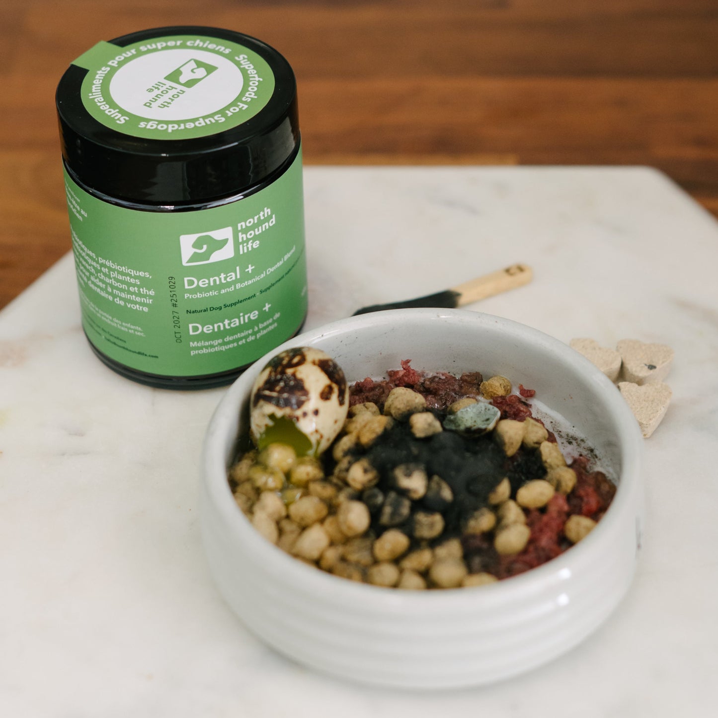 Green jar of Dental plus supplement for dogs on a marble surface next to a bowl of food.